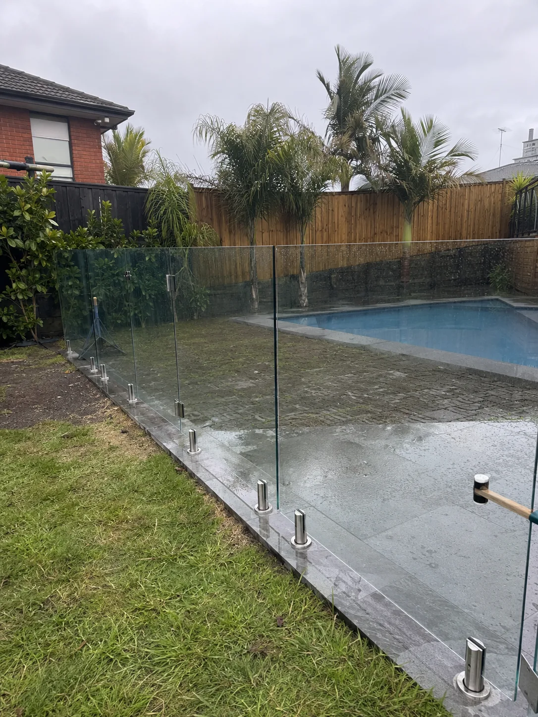 Frameless glass pool fence around a wet paved patio